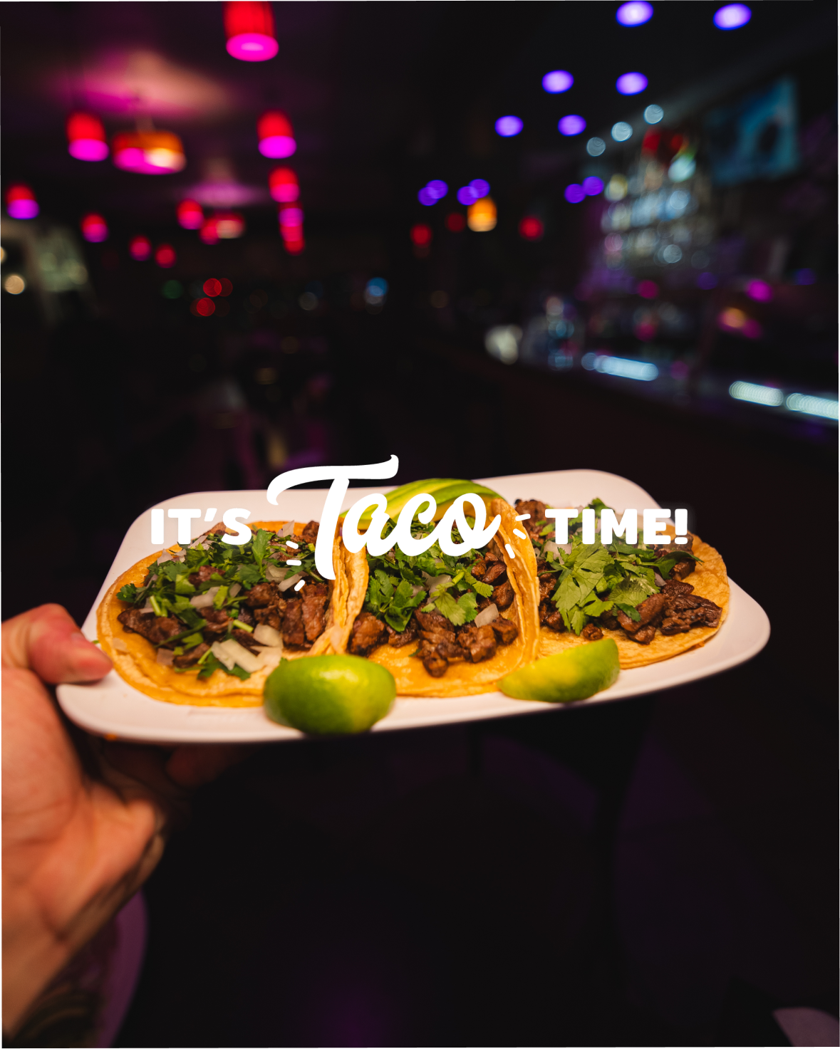 Three street tacos with carne asada, onion, cilantro and lime on a plate at a Taco Dále cantina