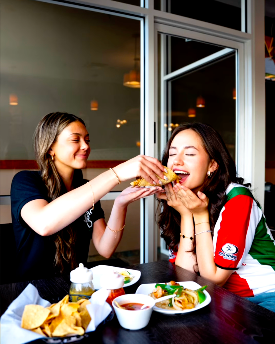 Two friends sharing tacos and chips at a Taco Dále table